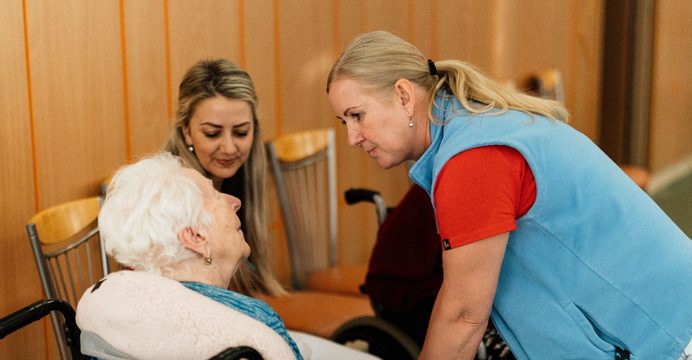 Two caregivers greeting a smiling resident in a wheelchair