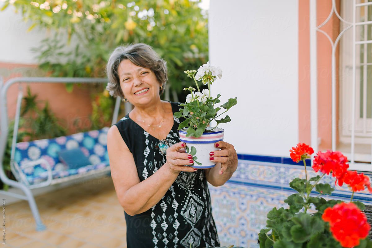 Rosa smiling on her patio, holding a pot of white geraniums