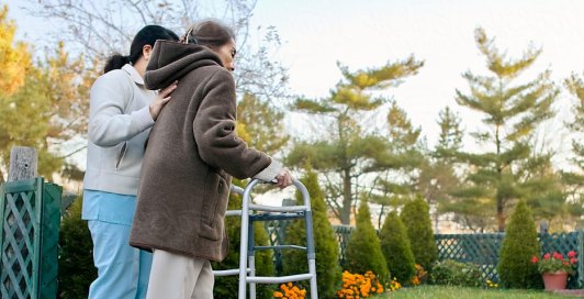 Caregiver helping a resident walk with a walker in the garden